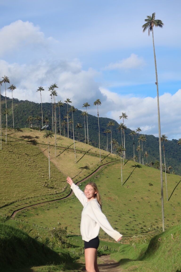 A traveler standing in Cocora Valley with towering wax palm trees in the background in Salento, Colombia. One of the best things to do in Salento. Colombia Travel Guide