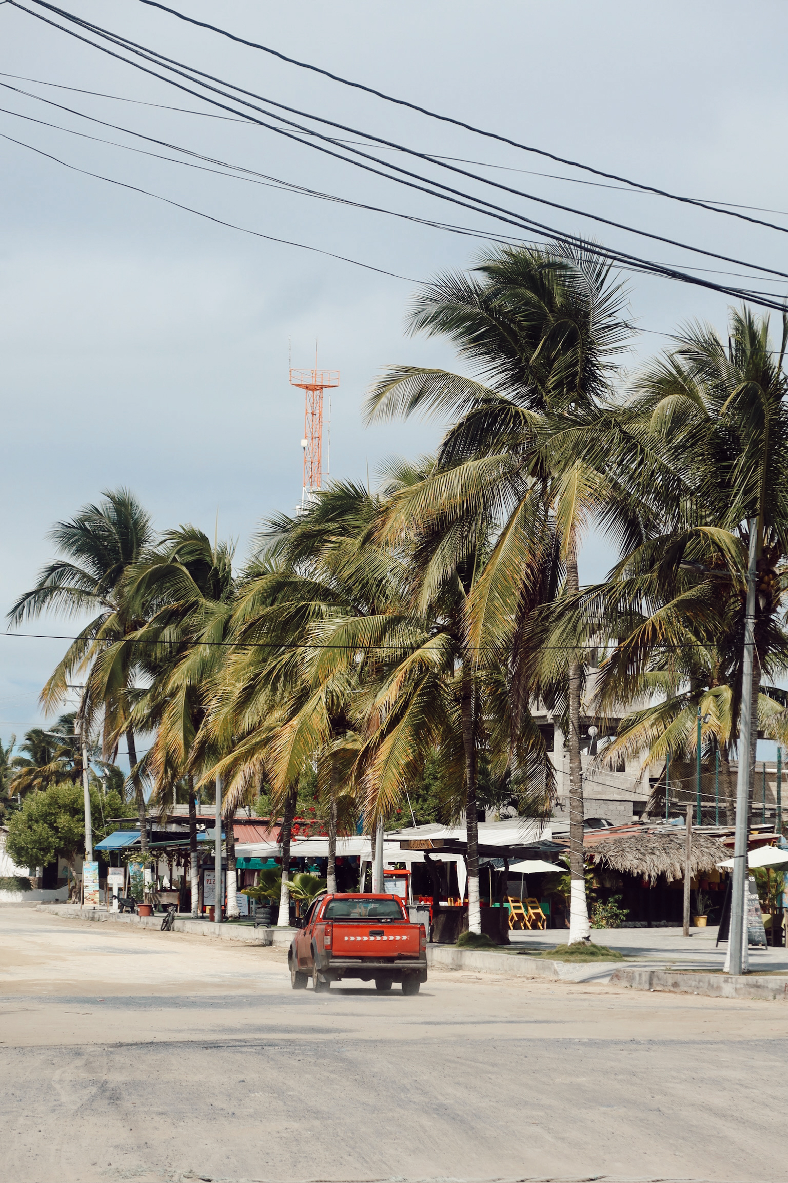 The quiet open town square featuring unpaved sandy streets, tall green palm trees and small local restaurant fronts.