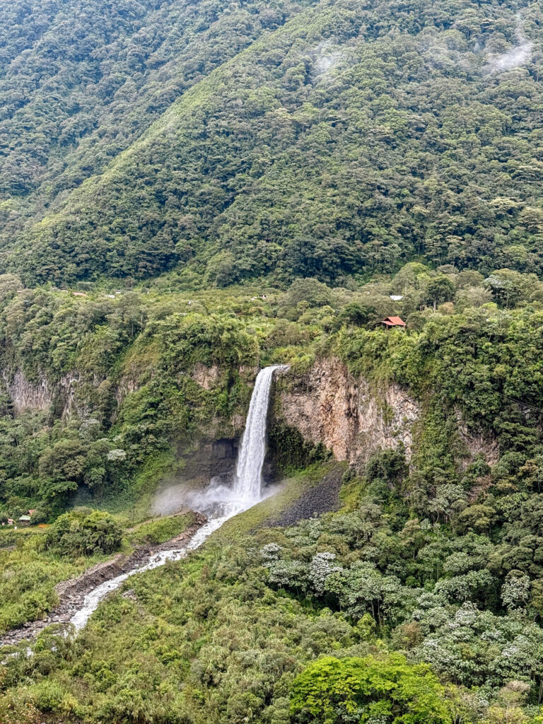 A tall, narrow waterfall plunging down a steep, jungle-covered cliffside along a mountain bike route