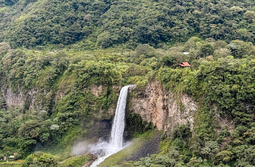 A tall, narrow waterfall plunging down a steep, jungle-covered cliffside along a mountain bike route