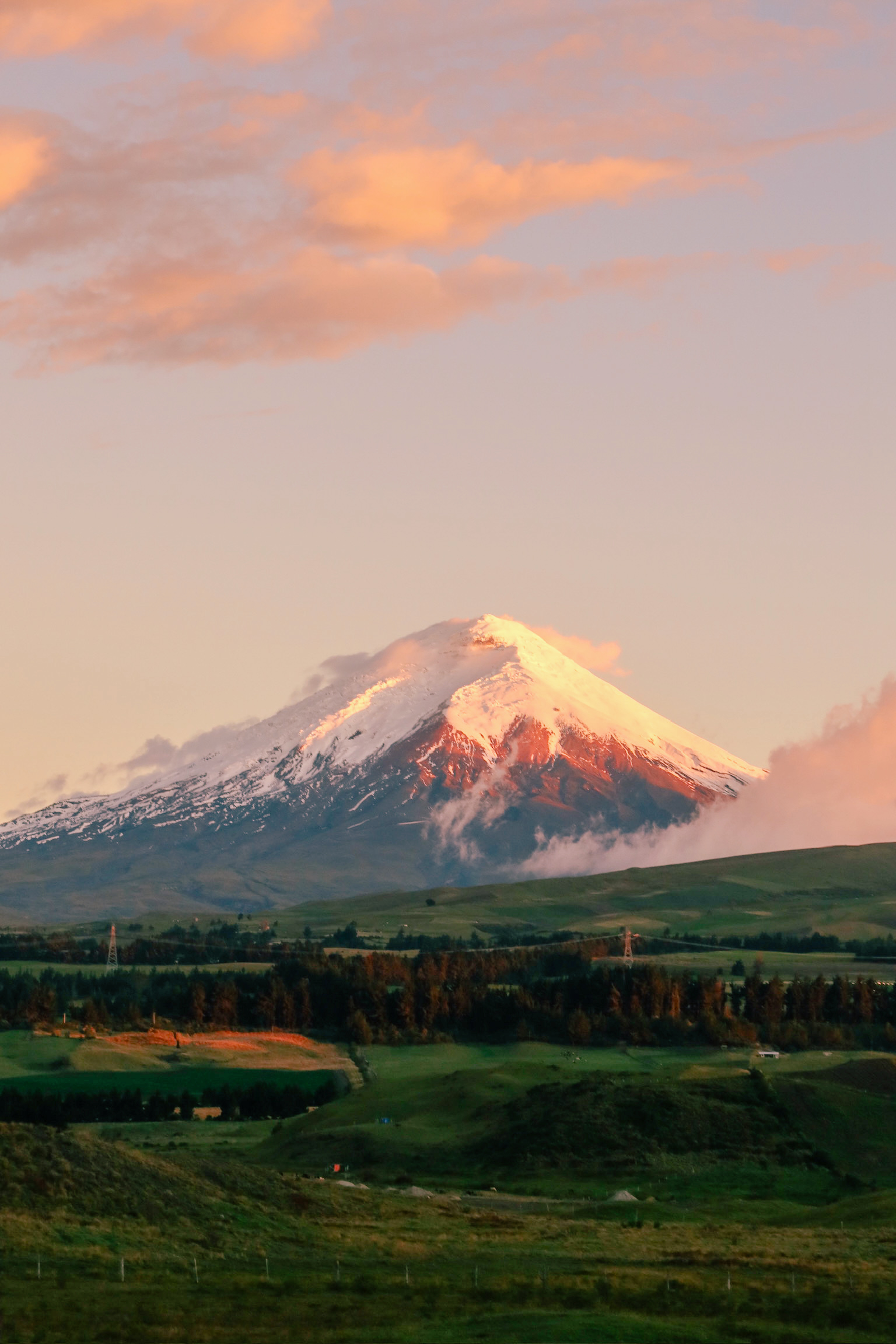 A dramatic sunset landscape view showing the snow capped peak reflecting the intense pastel pink and orange colours of the evening sky.