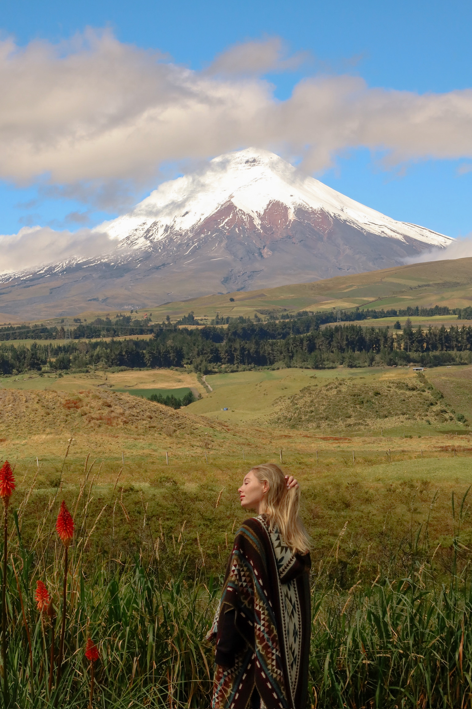 A full length travel portrait of me standing inside The Secret Garden Cotopaxi National Park with the giant symmetrical snow capped volcano rising directly behind me.