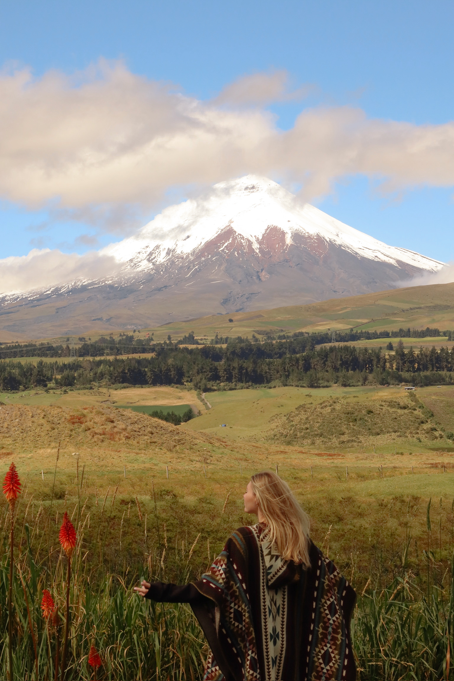 A medium shot of me smiling while wrapped inside a heavy grey and blue patterned traditional wool poncho with the volcano behind me.