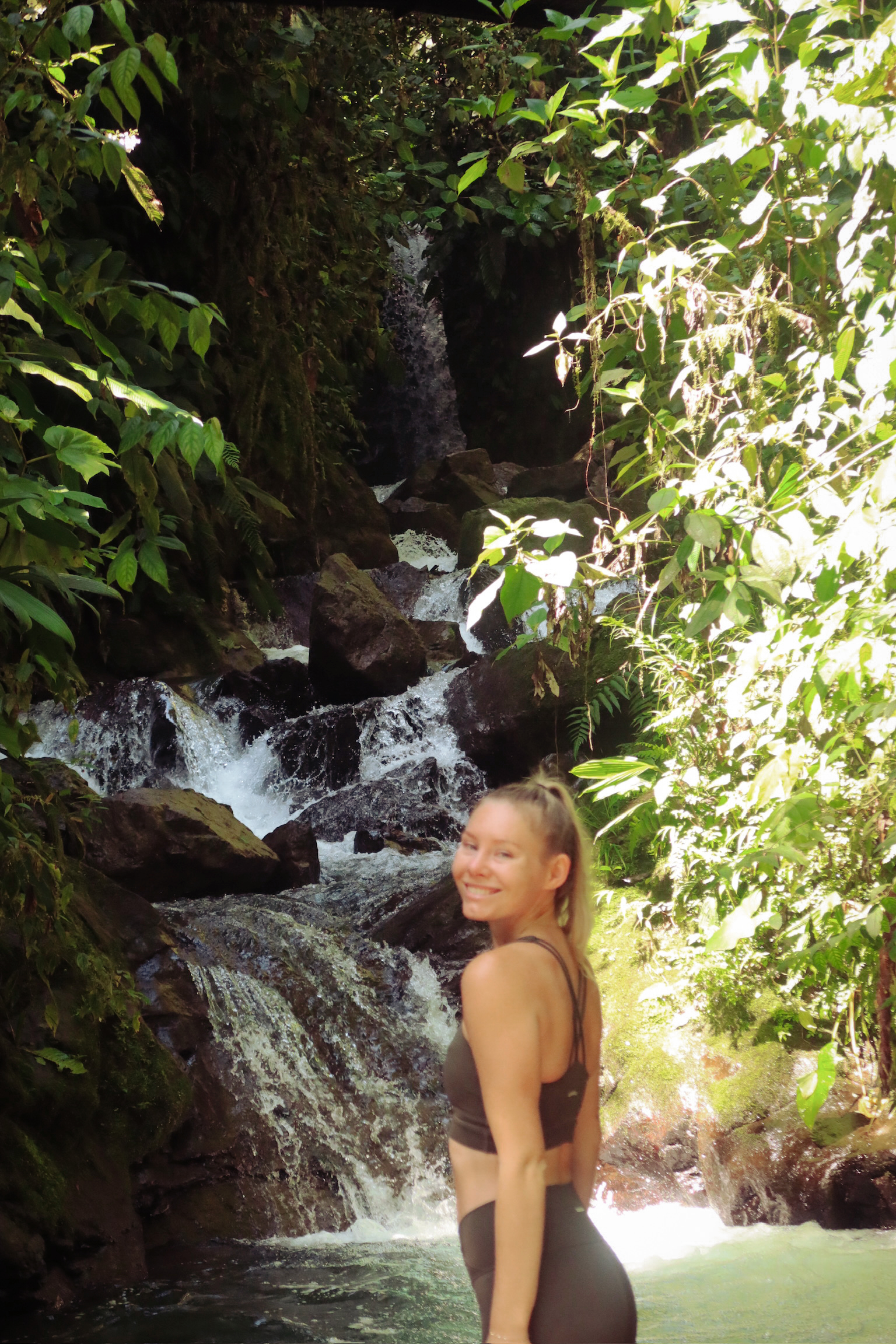 A portrait photo of me standing on a wet wooden viewing platform directly in front of a massive rushing tropical waterfall in Mindo.