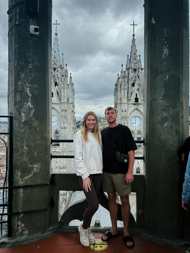 Me and Luke posing on a high stone ledge inside the Basilica del Voto Nacional with the 2 giant clock towers rising directly behind us.