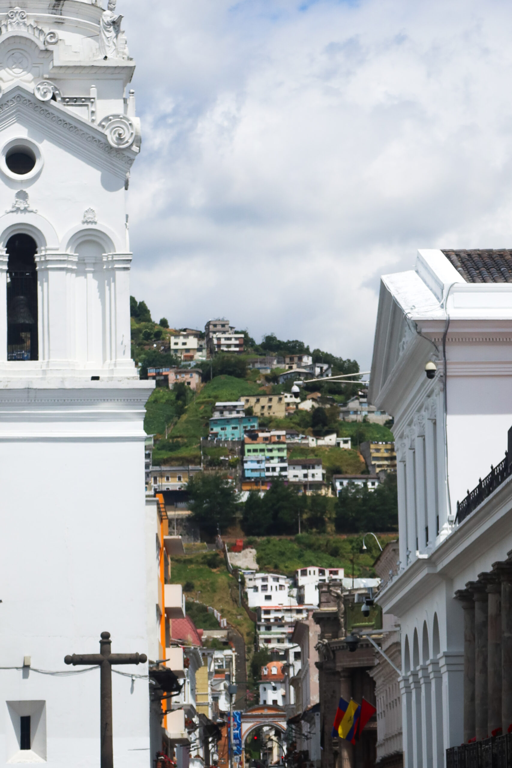 A panoramic viewpoint look at the steep green hillsides of Quito covered in hundreds of bright colourful houses under a blue sky.