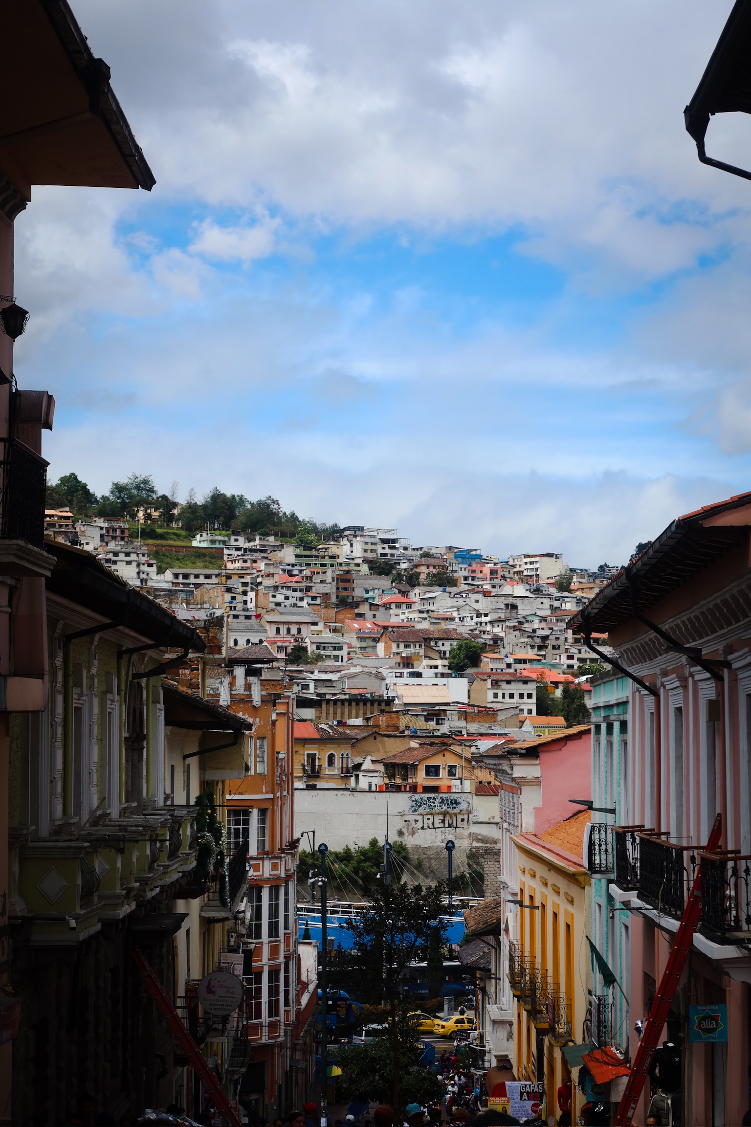 A ground level street view looking up a steep narrow cobblestone hill lined with historic colourful houses in old town Quito.