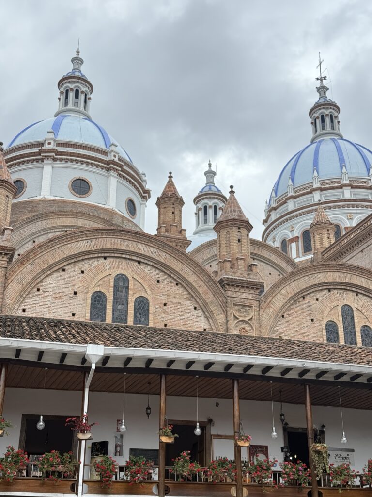 Low-angle view of the massive sky-blue tiled domes and towering facade of the New Cathedral against a bright blue sky in Cuenca, Ecuador.