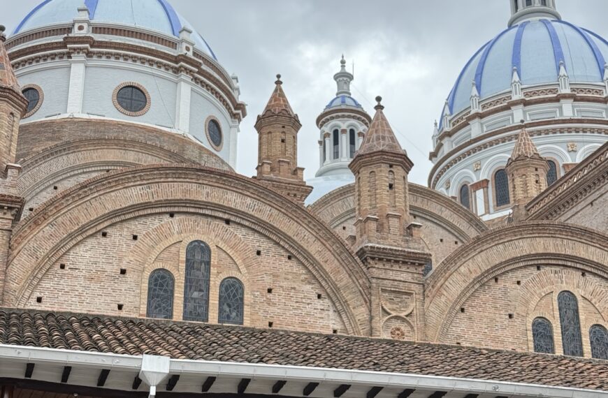 Low-angle view of the massive sky-blue tiled domes and towering facade of the New Cathedral against a bright blue sky in Cuenca, Ecuador.