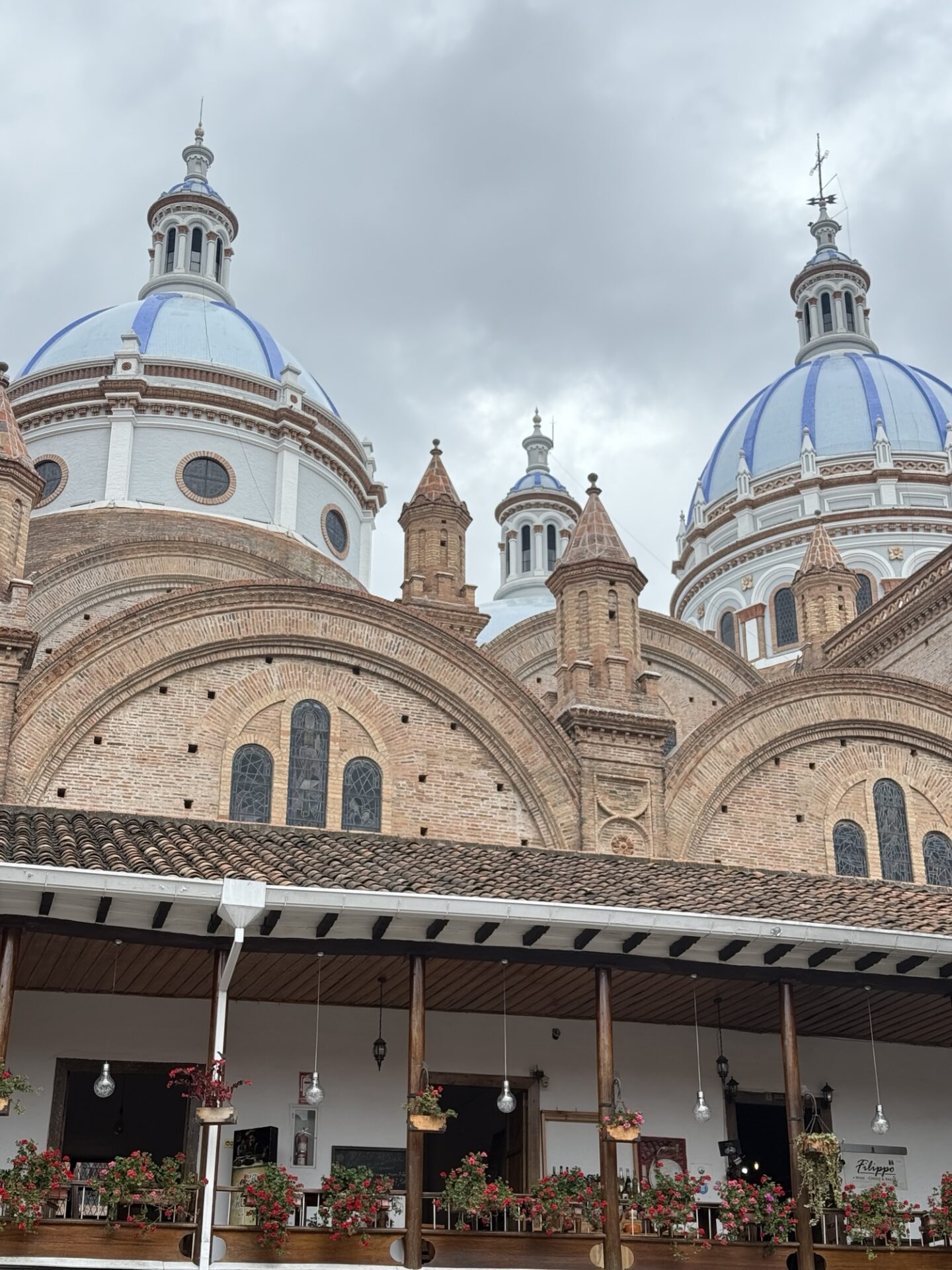Low-angle view of the massive sky-blue tiled domes and towering facade of the New Cathedral against a bright blue sky in Cuenca, Ecuador.