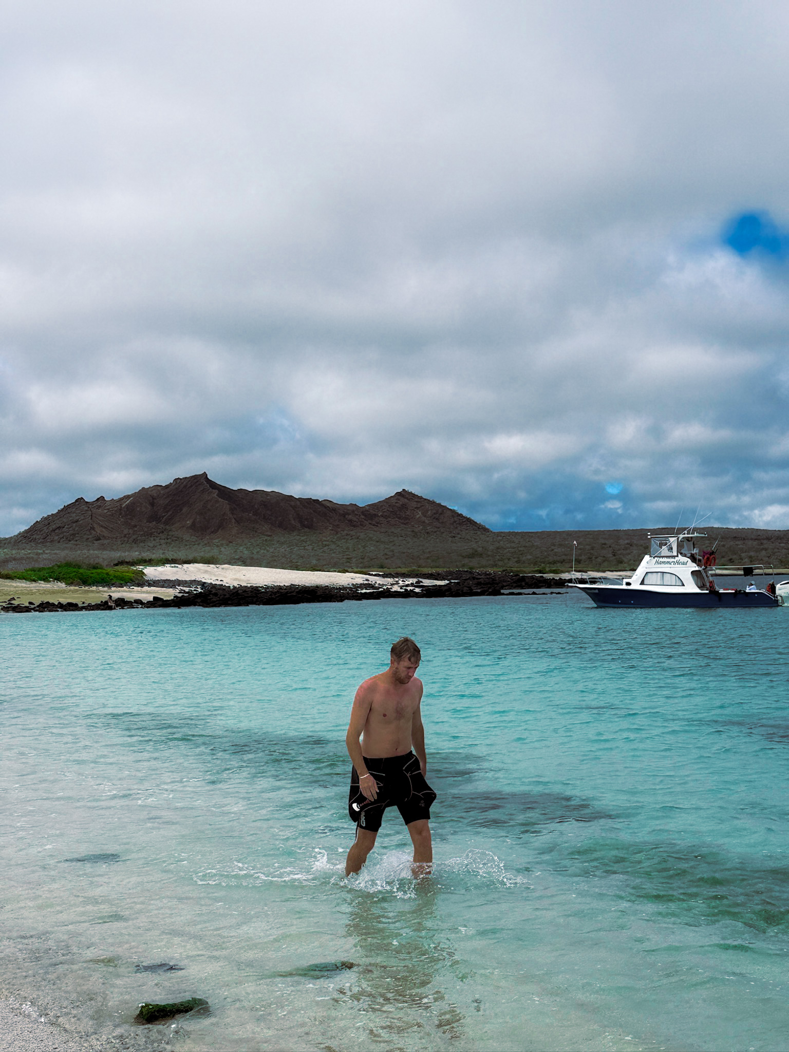 Luke walking through the shallow turquoise ocean water at the beach stop during the Kicker Rock tour.
